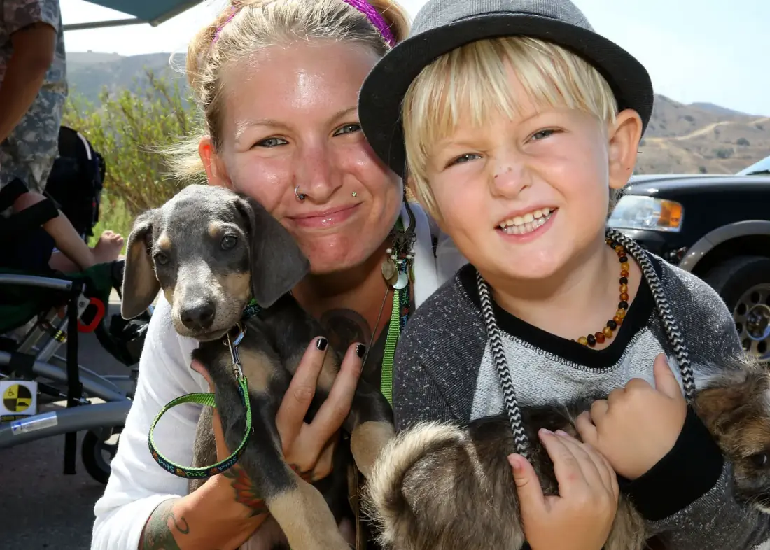 Una mamá y su hijo sonríen con dos cachorros que acaban de adoptar